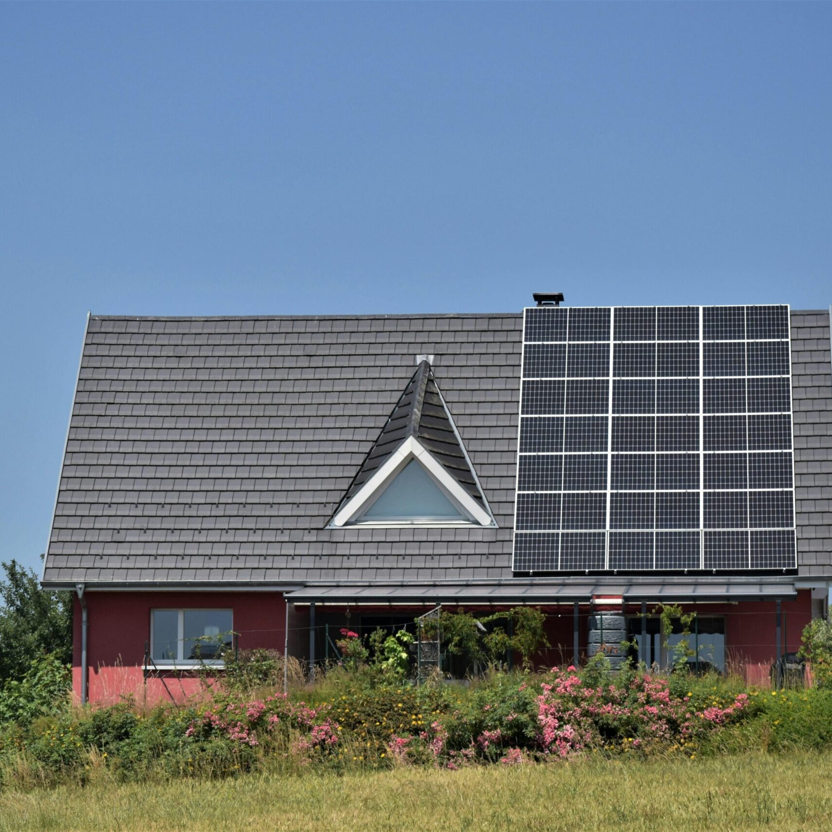 A modern house with solar panels and a garden, showcasing sustainability.